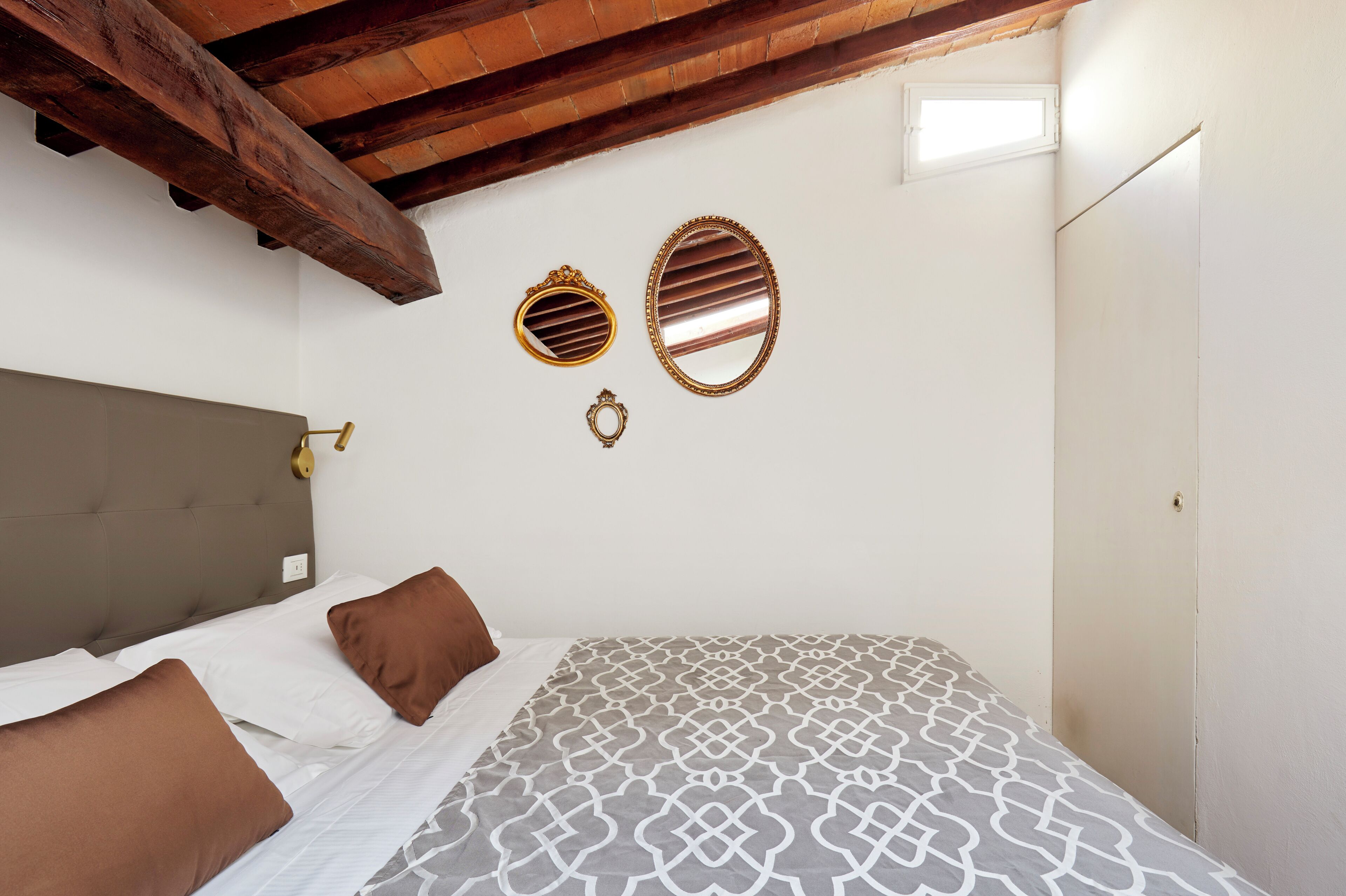 A bedroom with a bed, two wall mirrors, a wooden ceiling, and a white door.