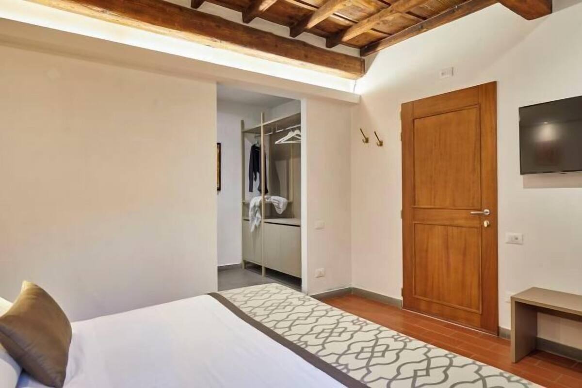 A bedroom with a bed, a wooden door, a wardrobe, and a television on the wall.