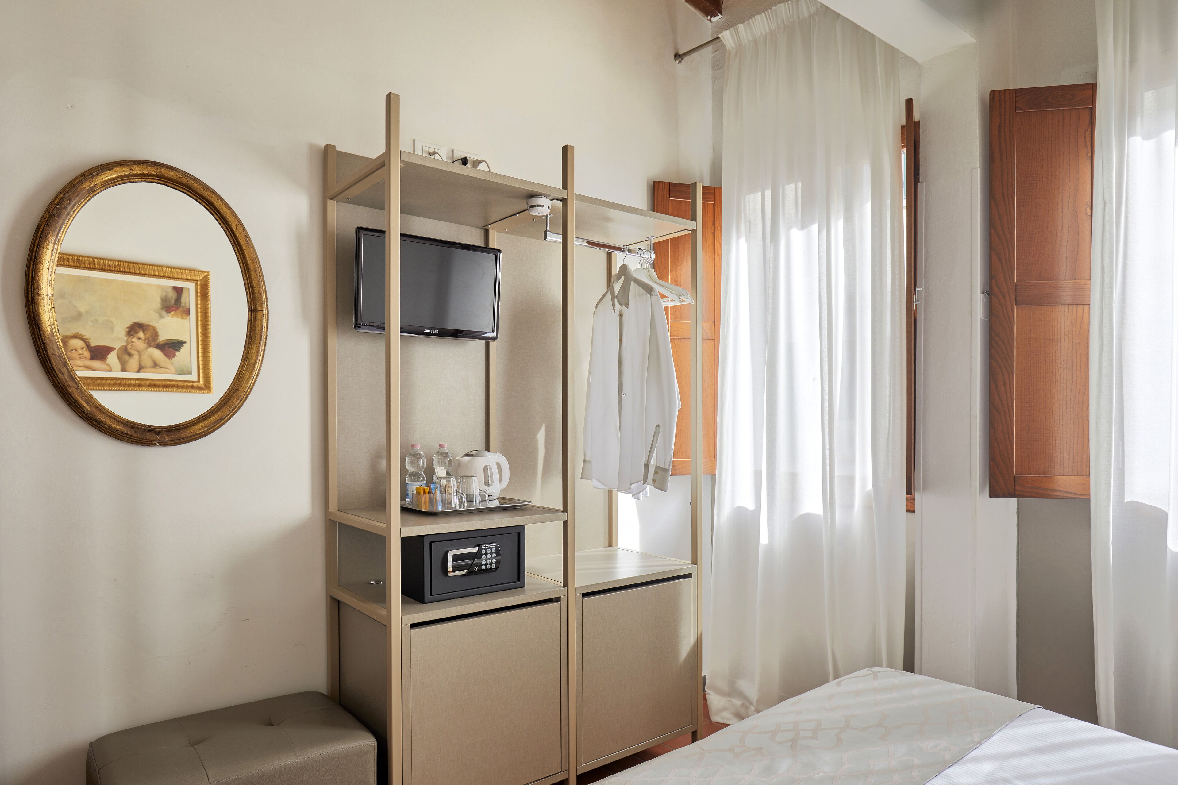 A hotel room with a bed, a TV, a minibar, a coat rack, and a mirror.