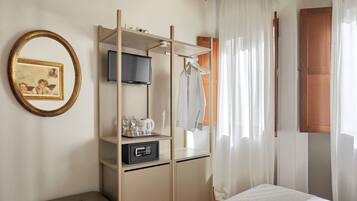 A hotel room with a bed, a TV, a minibar, a coat rack, and a mirror.