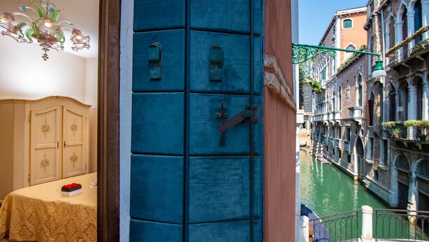 Una habitación con una cama, una mesa con una caja y vistas a un canal con edificios.