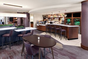Zona de bar moderna con barra, taburetes y un espacio de estar con mesa y sillas.