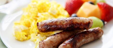 Un plato con huevos revueltos, salchichas y fruta.