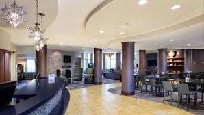 A spacious lobby with a curved reception desk, multiple seating areas, and a large television screen.