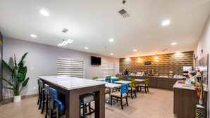 A modern dining area with a long counter, multiple chairs, and a kitchen in the background. - Clarion Pointe Madison Huntsville (Madison)