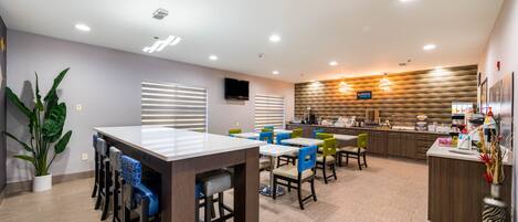 A modern dining area with a long counter, multiple chairs, and a kitchen in the background.