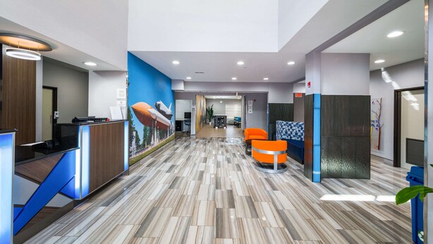 A modern reception area with a wooden reception desk, a blue accent wall, and a patterned floor. - Clarion Pointe Madison Huntsville (Madison)