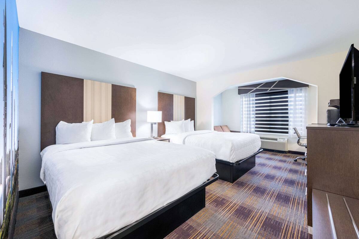 A hotel room with two beds, a desk, a chair, and a television.