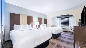 A hotel room with two beds, a desk, a chair, and a television.