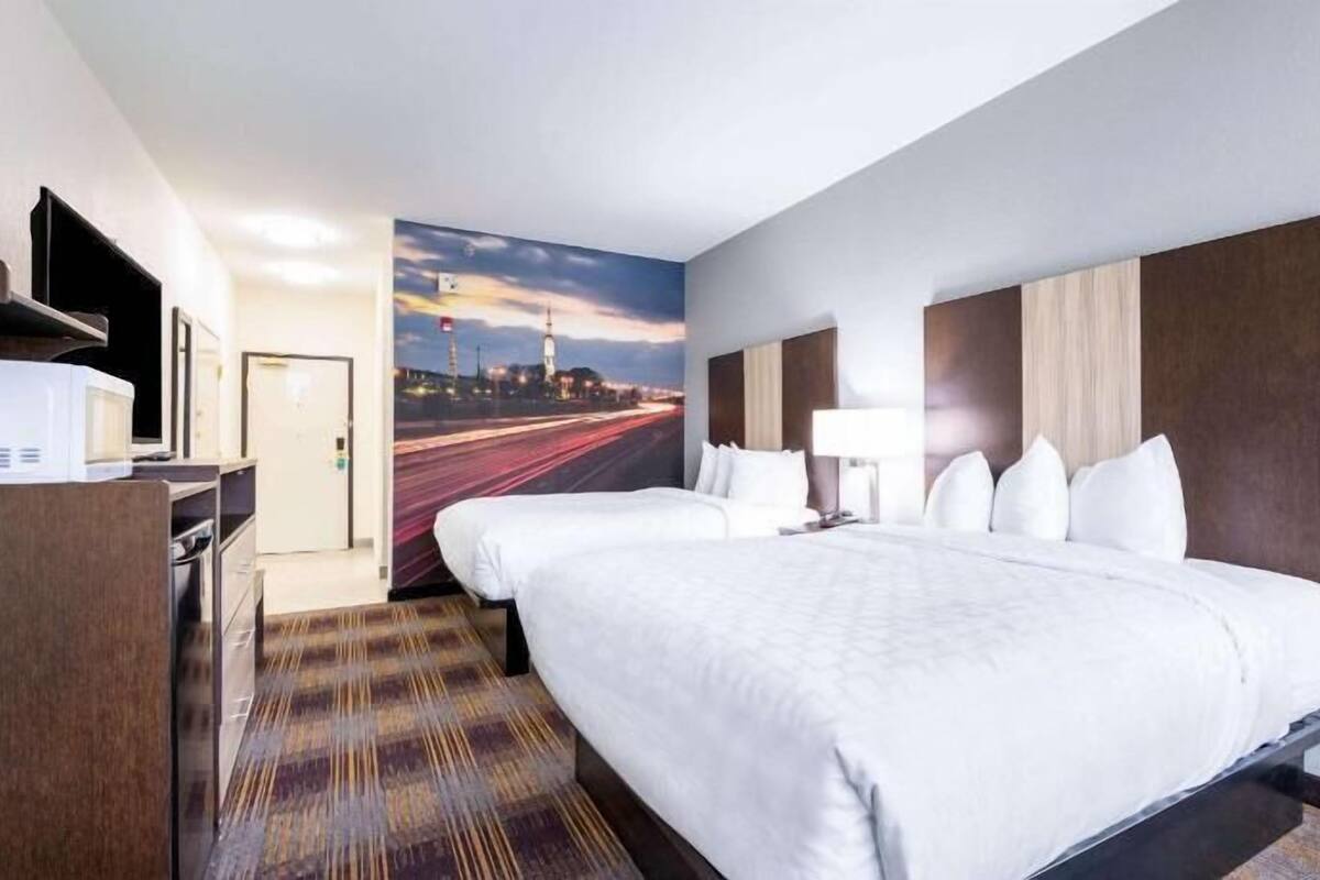 A hotel room with a bed, a desk, a TV, and a wall mural.