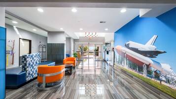 Um lobby moderno com um mural de ônibus espacial, assentos em azul e laranja e um chão limpo e bem polido.
