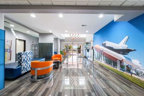 A modern lobby with a space shuttle mural, blue and orange seating, and a clean, polished floor. - Clarion Pointe Madison Huntsville (Madison)