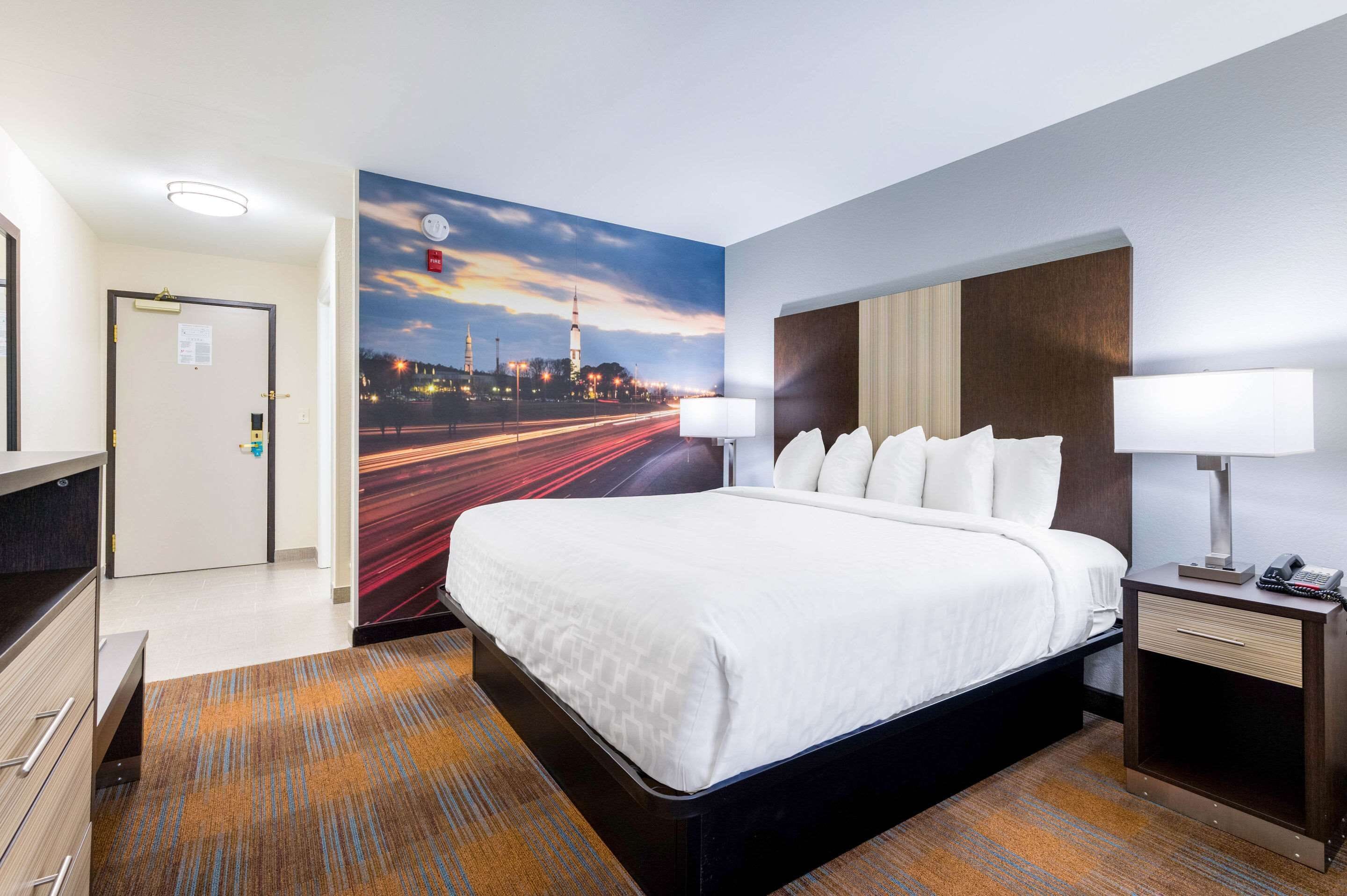 A hotel room with a large bed, two bedside tables, a nightstand, a desk, and a chair.