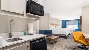 A hotel room with a kitchenette, a bed, a sofa, a desk, and a chair.