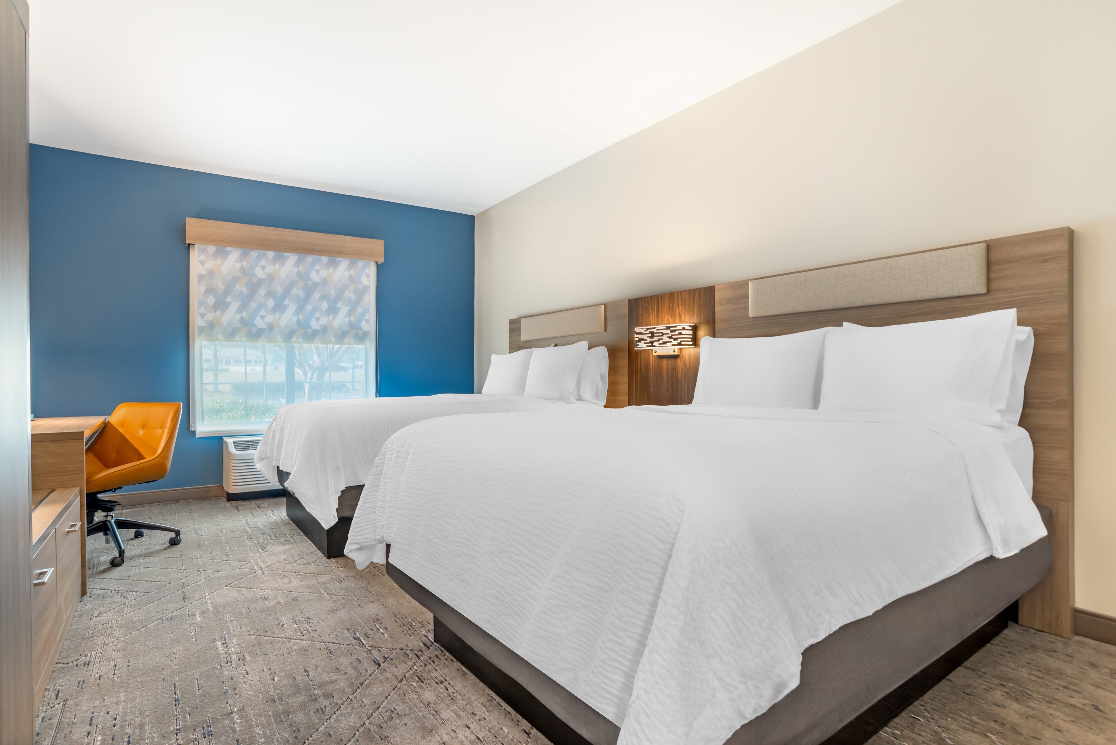 A hotel room with two beds, a desk, and a chair.