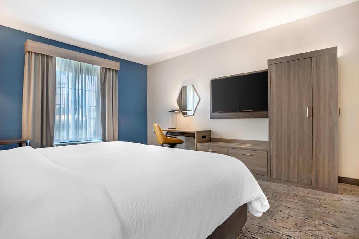 Ett hotellrum med en stor säng, ett skrivbord, en stol, en tv och en garderob.