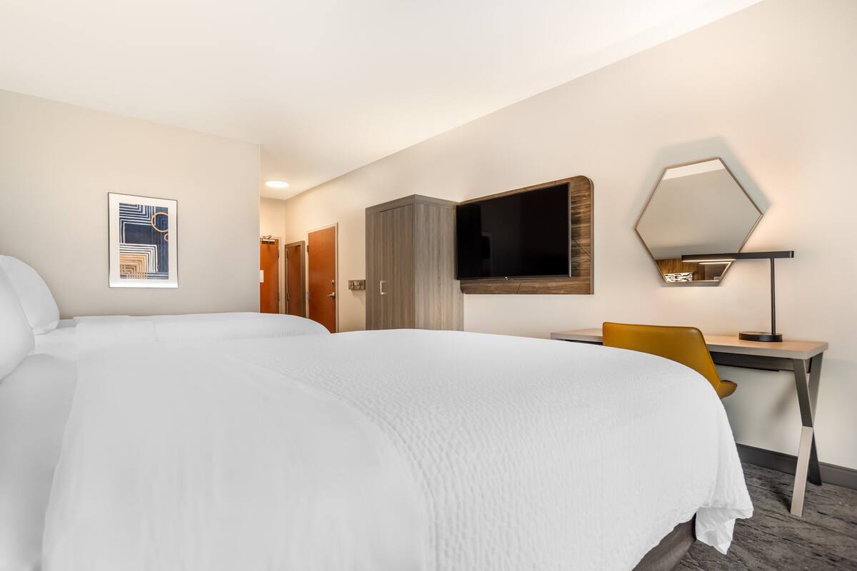 Ett hotellrum med en stor säng, ett skrivbord med en stol, en tv, en garderob och en spegel.