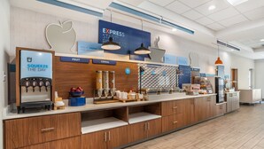 A modern breakfast bar with a beverage dispenser, cereal, and fruit display.
