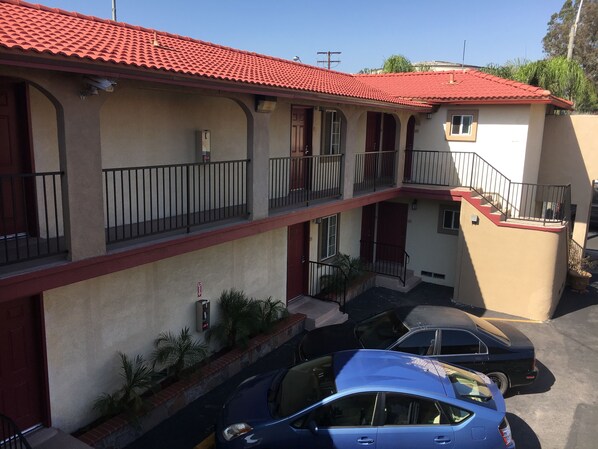 Un edificio de varios pisos con techo de tejas rojas, balcones y un estacionamiento con automóviles.