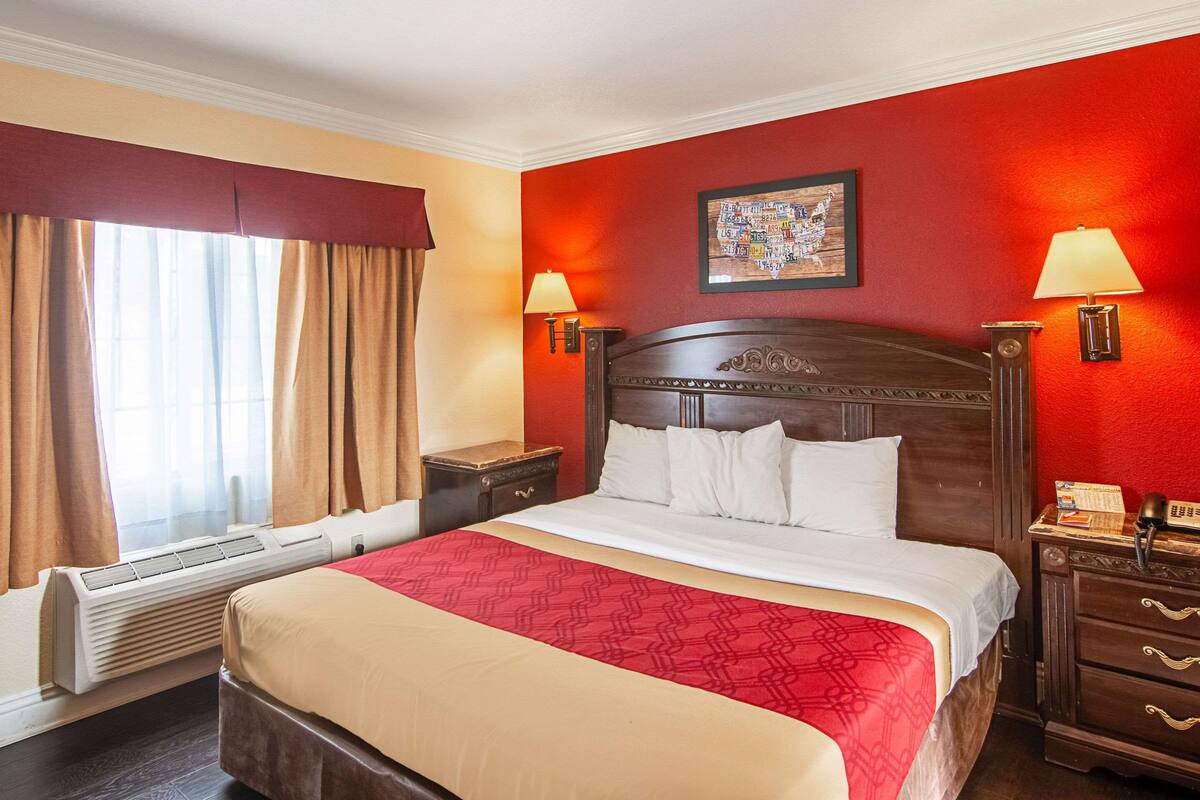 Habitación de hotel con una cama grande, un calentador, una mesita de noche y una lámpara fijada a la pared.