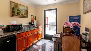 A hotel reception area with a wooden counter, a microwave, a framed painting, and a door leading outside.