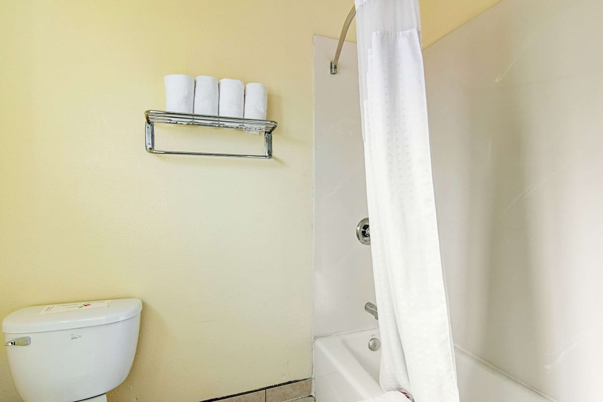 Un baño con inodoro, ducha con cortina y estante con toallas enrolladas.