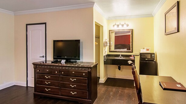 A hotel room with a wooden dresser, a television, a small table, a microwave, and a sink with a mirror above it.
