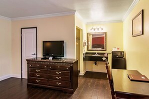 Une chambre d’hôtel avec une commode en bois, un téléviseur, une petite table, un four à micro-ondes et un lavabo avec un miroir au-dessus.