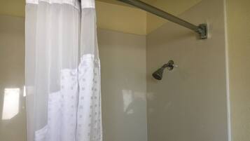 Un espacio de ducha con cabezal, un inodoro blanco y una cortina.