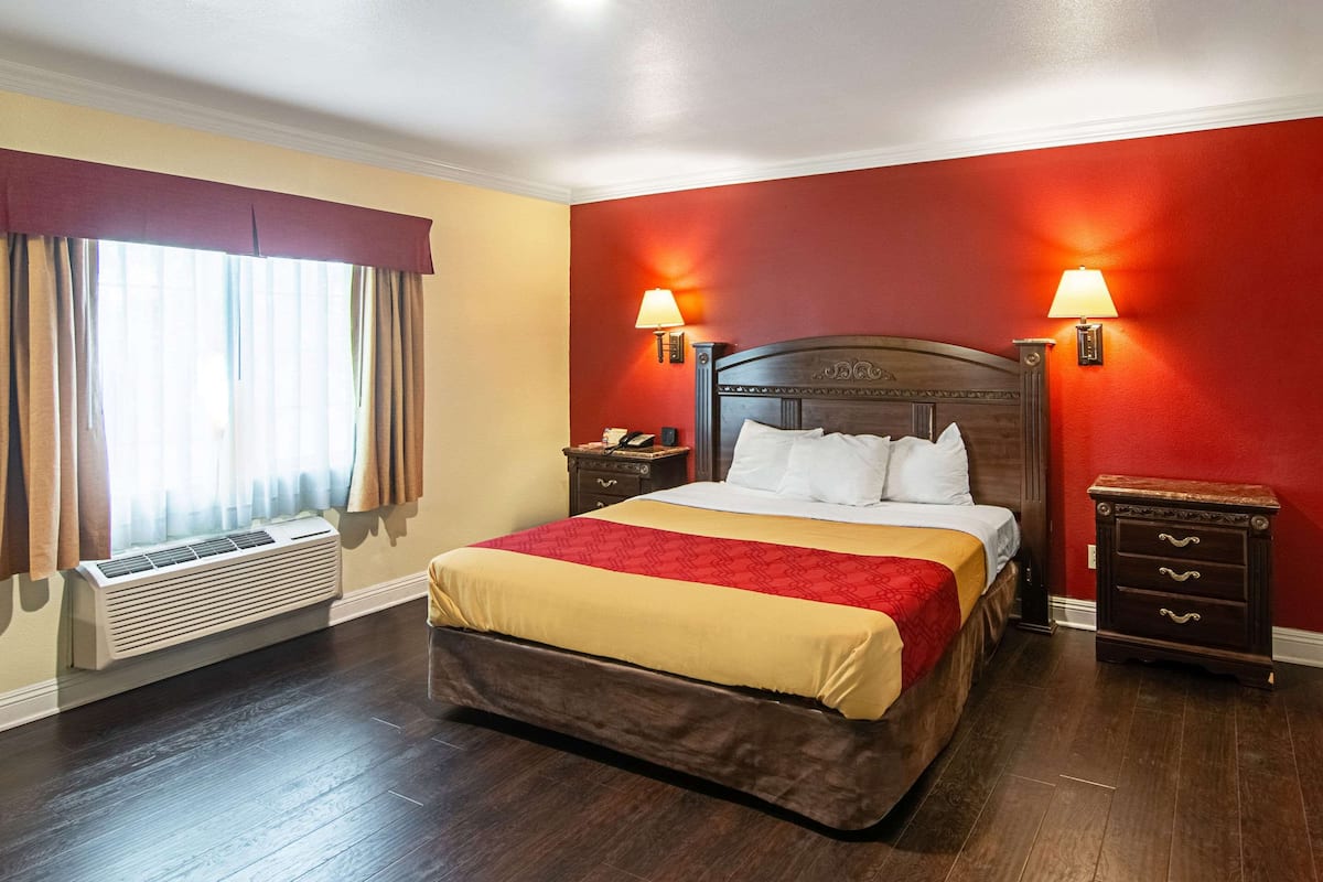 Una habitación de hotel con una cama grande, dos mesitas de noche, un ventanal con cortinas y un equipo de aire acondicionado.