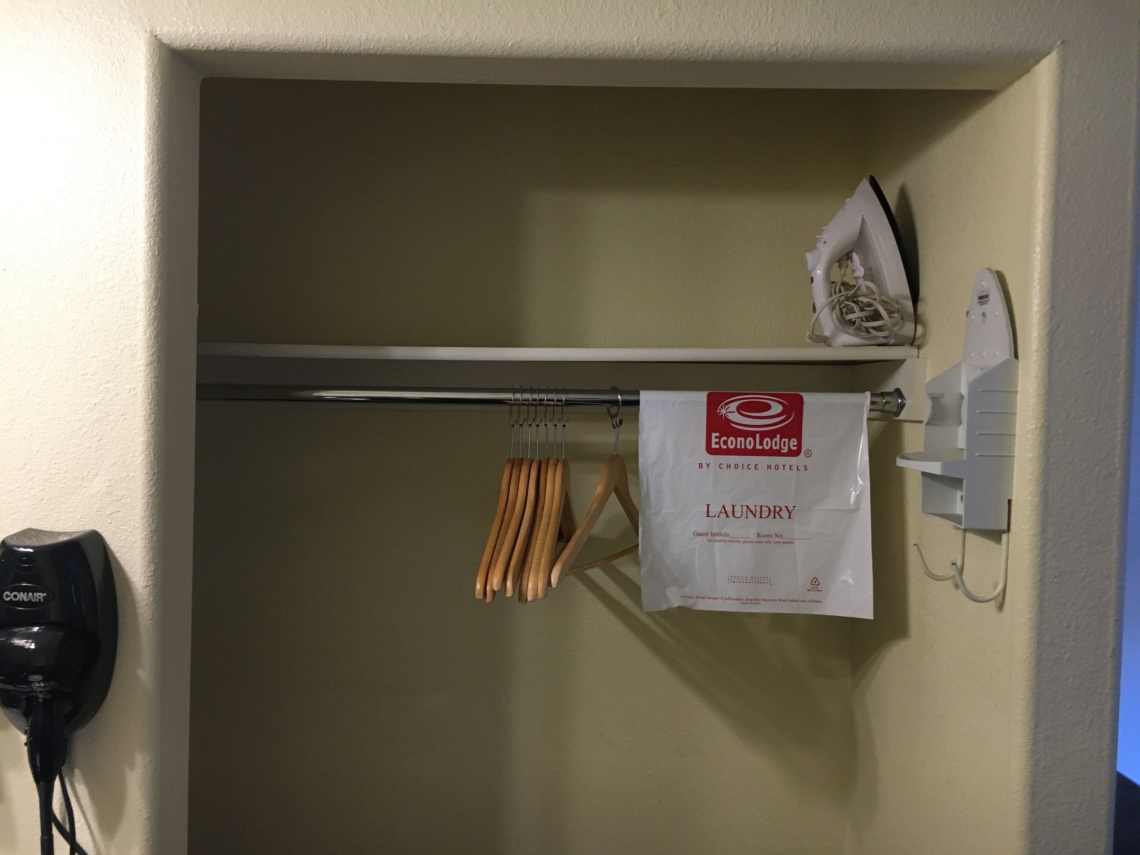 A hotel bathroom with a towel rack, a hand dryer, and a laundry bag hanging on the wall.