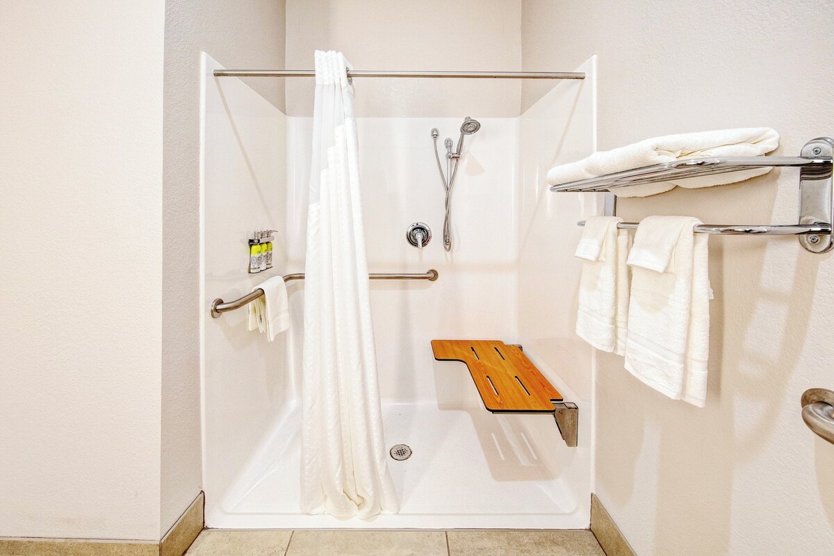 Une douche à l’italienne avec une porte en verre, un banc en bois à l’intérieur de la douche et un porte-serviettes avec des serviettes.