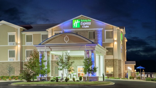 Edificio de Holiday Inn Express & Suites con una entrada bien iluminada, un área exterior cubierta y un jardín delantero ajardinado.