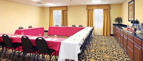 Un salón de conferencias con mesas dispuestas para reuniones, una estación de café y suelo con alfombra estampada.