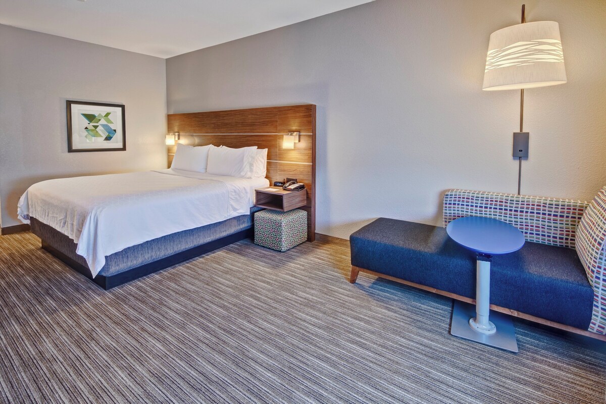 Une chambre d’hôtel avec un grand lit, une table de chevet, une lampe et un petit coin salon avec une table.
