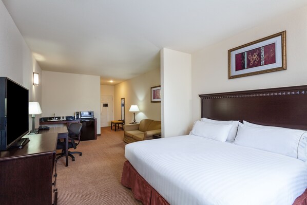 Habitación de hotel con una cama grande, un escritorio con computadora, una silla, televisor y un cuadro en la pared.