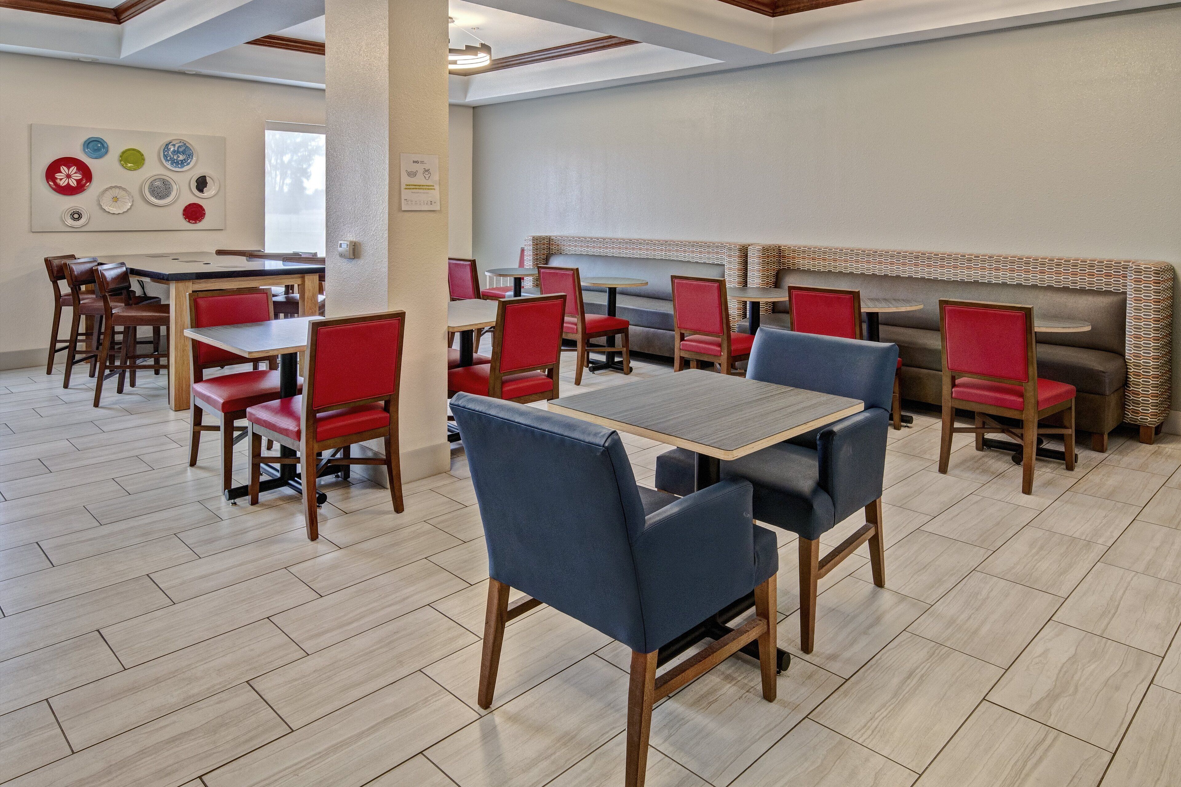 Un restaurante con mesas de madera, sillas rojas, un banco de mimbre y piso de baldosas.