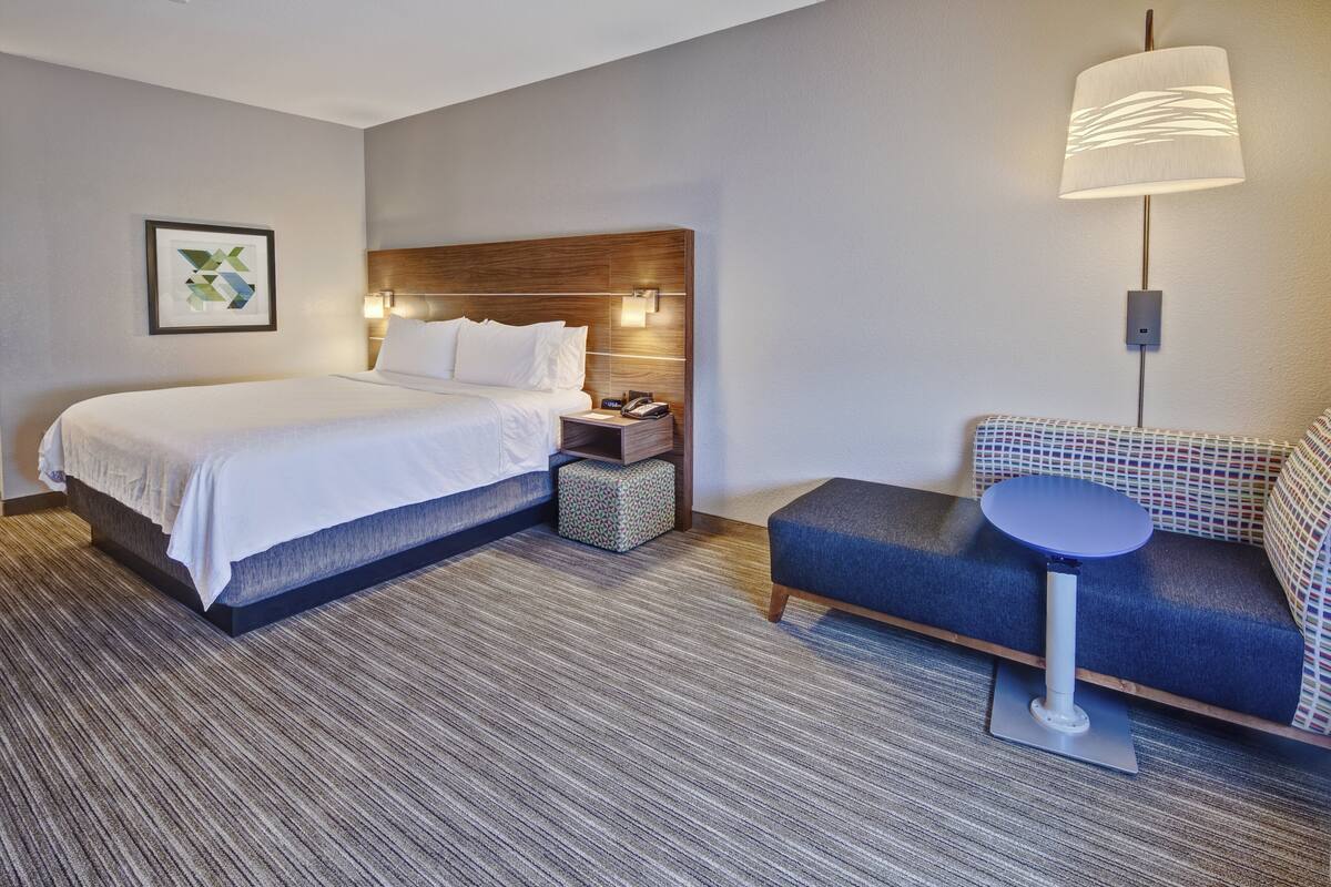 Ein Hotelzimmer mit einem großen Bett, Nachttisch, Lampe und einer kleinen Sitzecke mit Tisch.