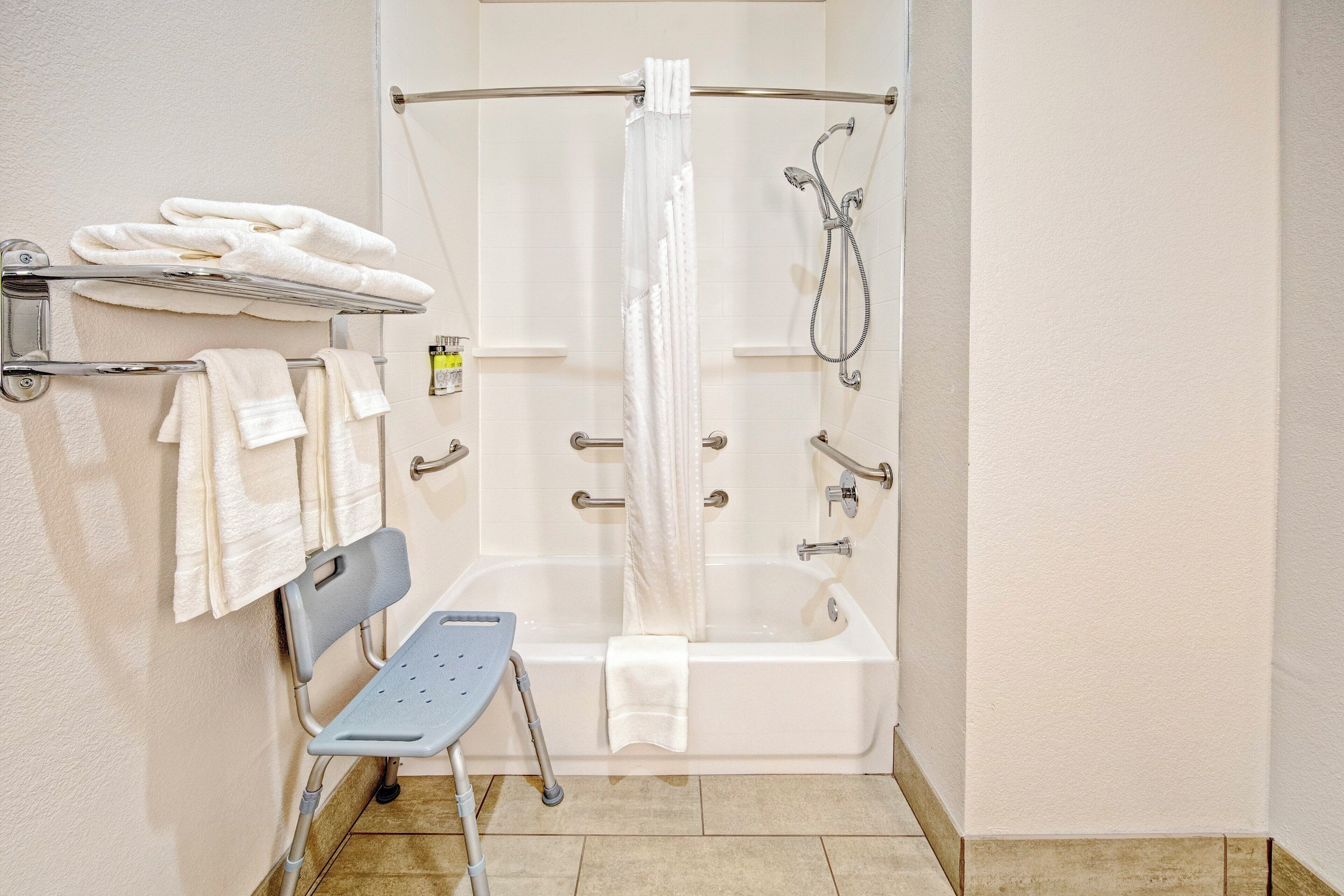 A bathroom with a glass-enclosed shower, a bathtub, a grab bar, and a shelf with towels.