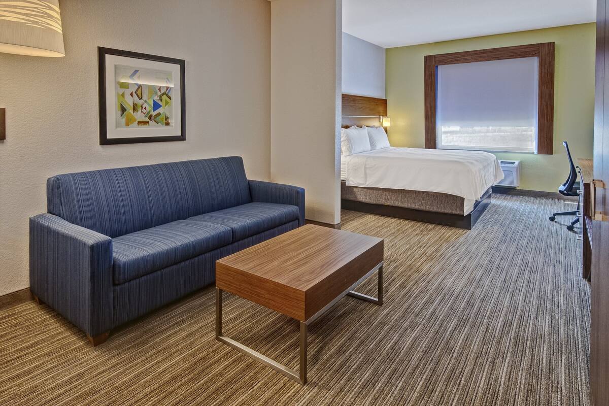 Ein Hotelzimmer mit einem blauen Sofa, einem Holztisch, einem Bett mit weißer Bettwäsche und einem großen Fenster.