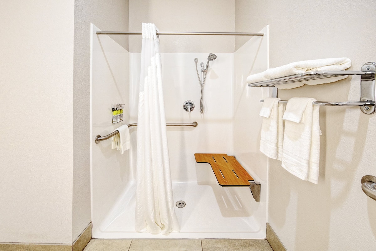 Eine begehbare Dusche mit Glastür, eine Holz-Duschbank und ein Handtuchhalter mit Handtüchern.