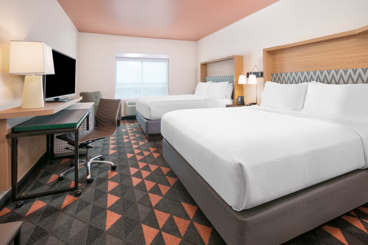 A hotel room with two beds, a desk with a computer, a chair, and a TV.