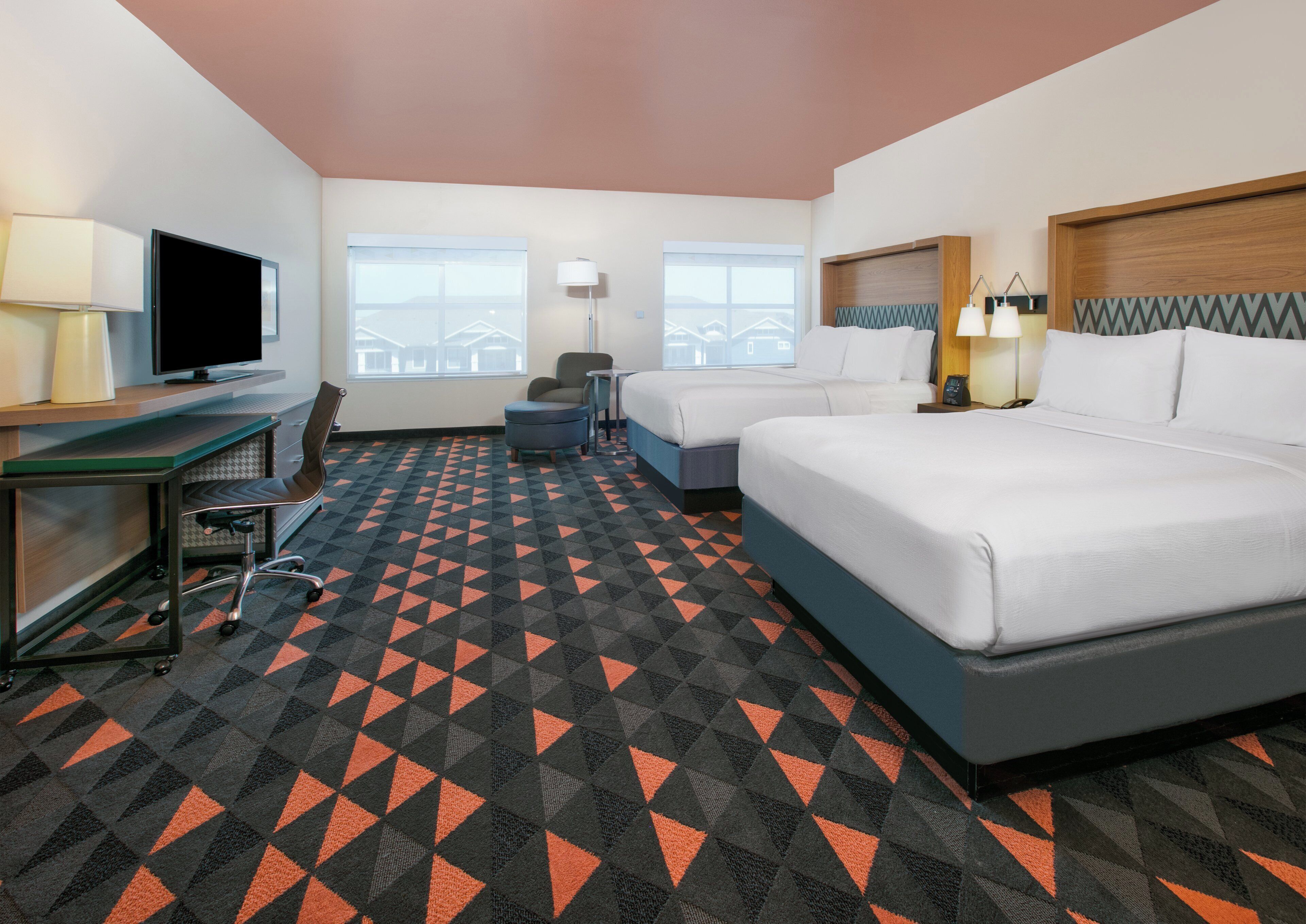 A hotel room with a bed, desk, chair, and a TV.