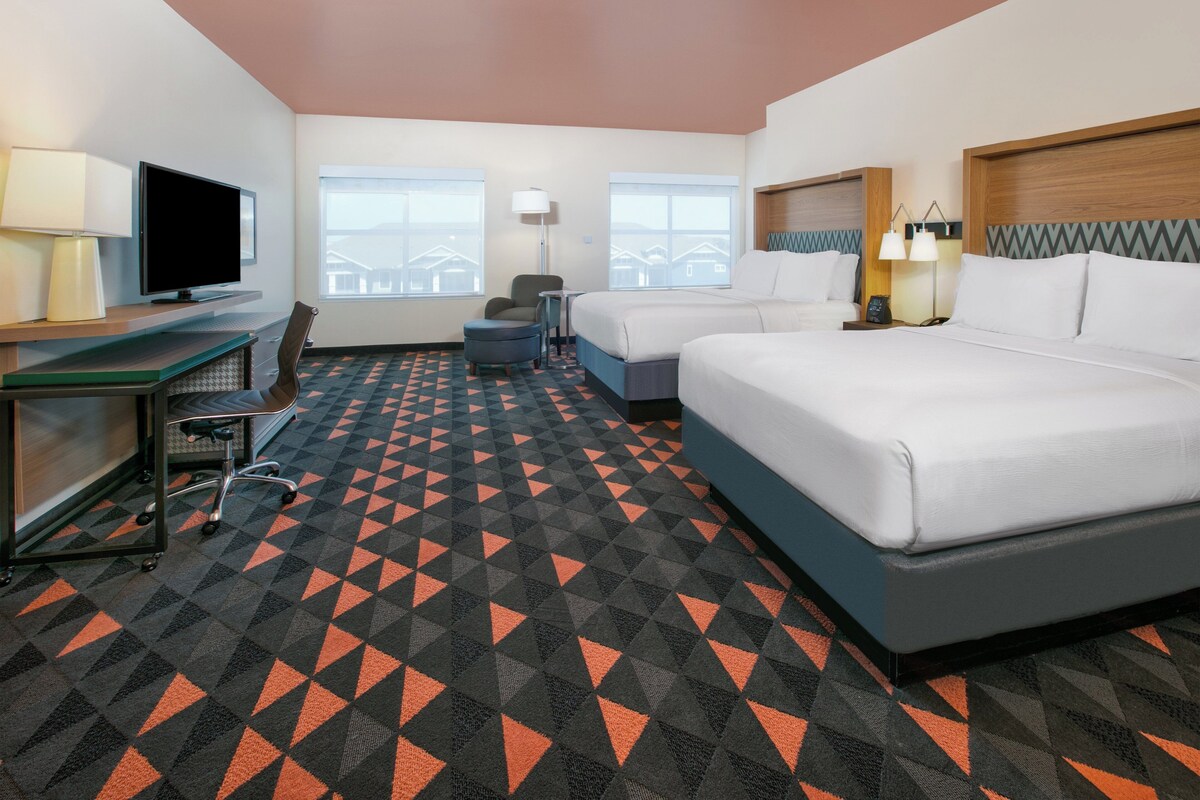 A hotel room with a desk, two beds, a chair, and a TV.