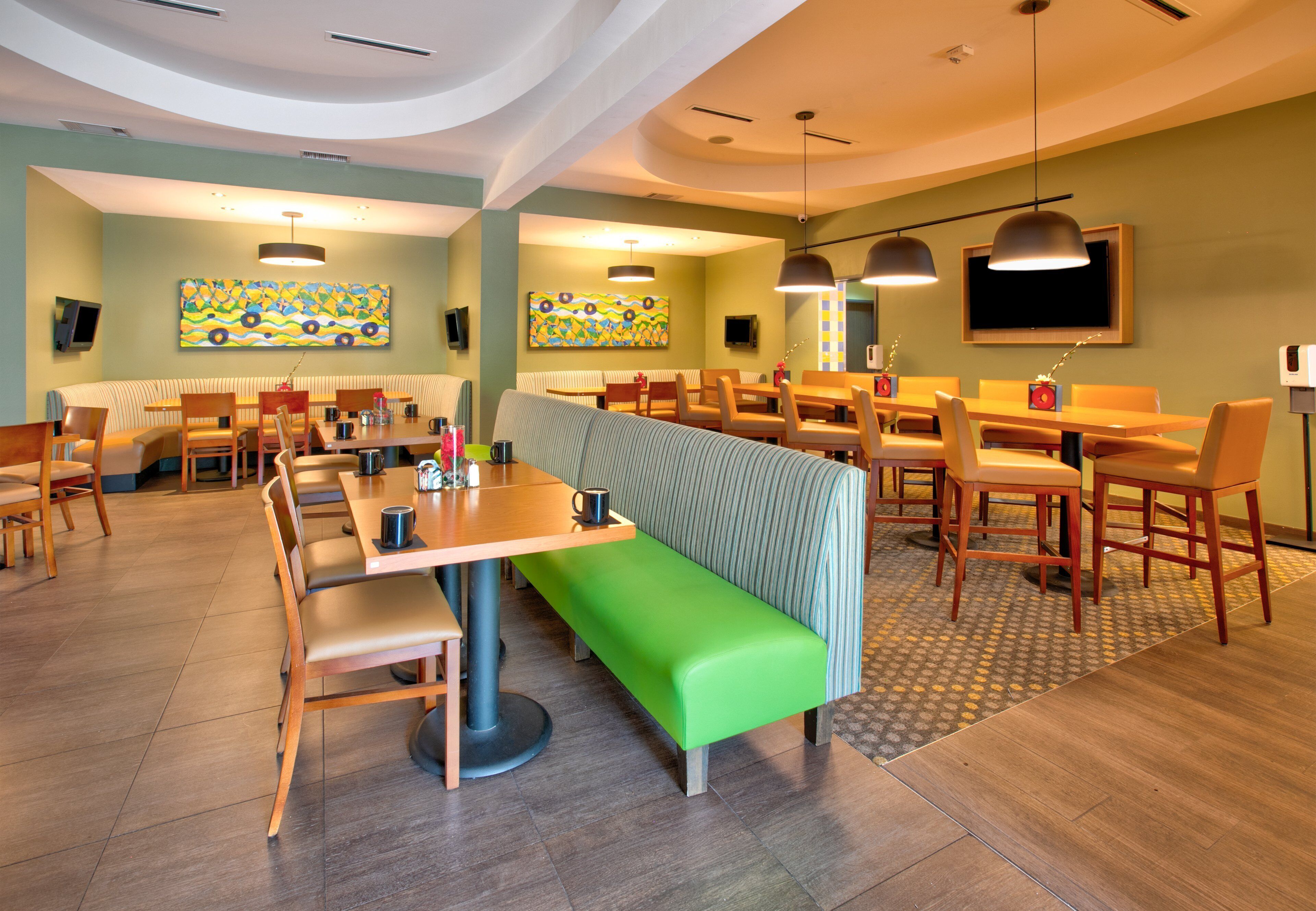 Un espace repas moderne avec des banquettes et des tables, un banc vert et des œuvres d’art accrochées aux murs.