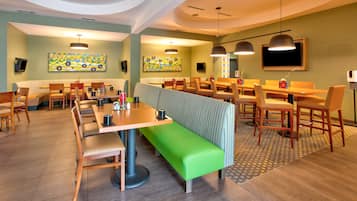 Un espace repas moderne avec des banquettes et des tables, un banc vert et des œuvres d’art accrochées aux murs.