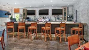 Zona de bar moderna con una barra larga, varios taburetes y un área de estar con una mesa y sillas.