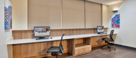 A modern office space with two desks, each with a computer and a chair. There are cabinets below the desks and a large artwork on the wall.