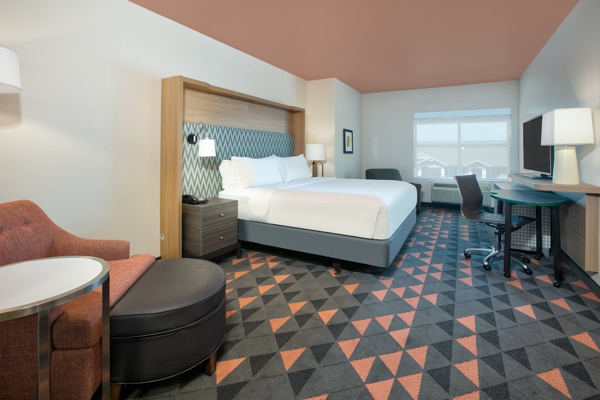 A hotel room with a bed, desk, chair, and a small table.