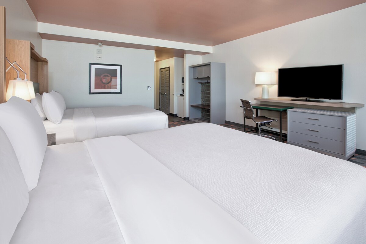 A hotel room with two beds, a desk, a television, and a picture on the wall.